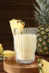 Tasty pineapple smoothie in glass and slices of fruit on wooden table, closeup