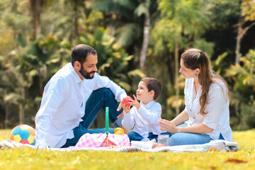 Brazilian family enjoying a happy picnic outdoors. The young boy holding an apple, emphasizing healthy eating and family bonding. Ideal for themes of love, wellness, and joyful moments together.