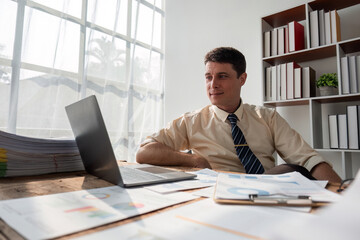 Young Businessman Sitting and Working in a Modern Office with Documents and Laptop on Desk