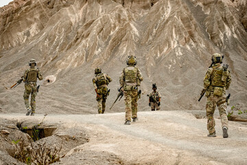 A group of military men in combat gear patrol in the middle of a desert and tropical jungle....