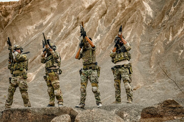 A group of military men in combat gear patrol in the middle of a desert and tropical jungle....