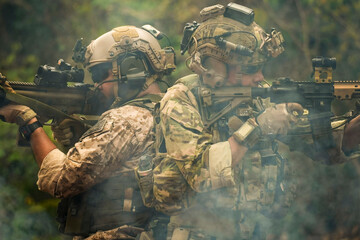 A group of military men in combat gear patrol in the middle of a desert and tropical jungle....