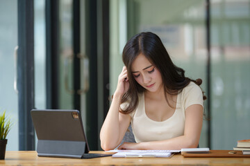 Seriously, a young woman working with paperwork and a digital tablet in the office.