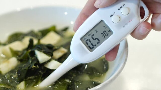 실내에서 측정기로 미역국의 염도를 테스트하는 손