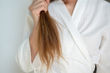 Cropped shot view of woman holding her split ends hair. Split ends happen when the ends of your hair become dry, brittle, and frayed.