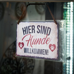 Schild mit der deutschen Aufschrift hier sind Hunde willkommen, an einem Geschäft für Hundemode...