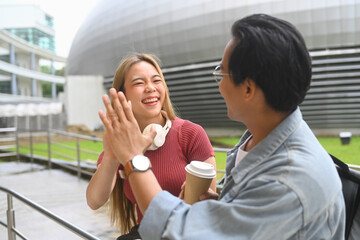 Cheerful students giving high five greeting each other in front of university building