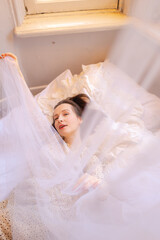 Morning of beautiful young woman lying in bed and streching. Girl in dress waking up under canopy in bedroom. Light vertical shot of sleeping beauty. Dreaming lady 