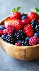 A wooden bowl filled with a variety of fresh, colorful berries including strawberries, raspberries, blueberries, and blackberries.