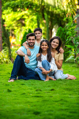Fototapeta premium Happy Indian family of four sitting in park, embracing and smiling at camera, enjoying quality time