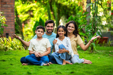 Fototapeta premium Happy Indian family of four sitting in park, embracing and smiling at camera, enjoying quality time