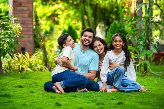 Happy Indian family of four sitting in park, embracing and smiling at camera, enjoying quality time