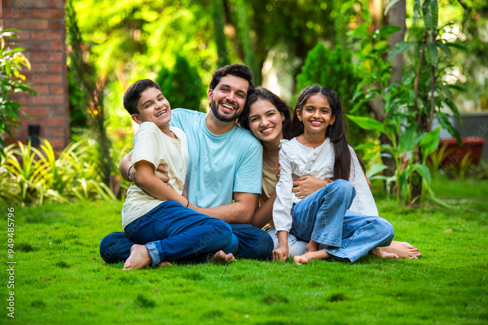 Wall mural Happy Indian family of four sitting in park, embracing and smiling at camera, enjoying quality time