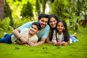 Fototapeta premium Happy Indian family of four sitting in park, embracing and smiling at camera, enjoying quality time