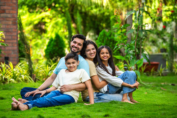 Fototapeta premium Happy Indian family of four sitting in park, embracing and smiling at camera, enjoying quality time