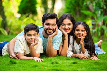 Happy Indian family of four sitting in park, embracing and smiling at camera, enjoying quality time