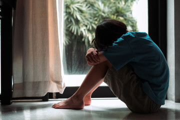 Crying girl, victim of bullying, abuse, violence, depressed patient, offering psychotherapy sitting on floor near door in the room. She was bullied, unhappy, upset, feel sick. Lonely concept.