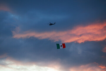 Ciudad de Mexico, Mexico - November 30. 2023: Helicopter in flight shows a Mexican Flag to people on the ground during a cloudy day