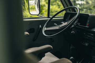 Drivers position of an old vintage van. Big plastic steering wheel and captain seats visible in a...