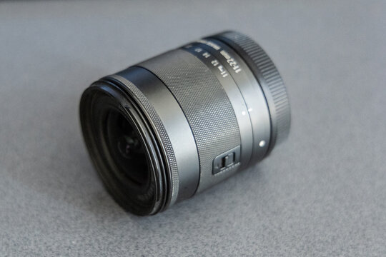 Small wide angle lens in size of 11-22mm, lying on the ground. Lens of small size without lens cap on. Zoom lens photography apparel.