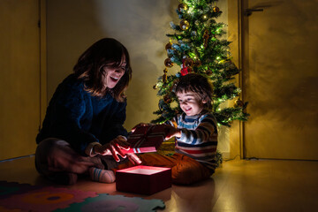 A woman and a child are opening a present in front of a Christmas tree