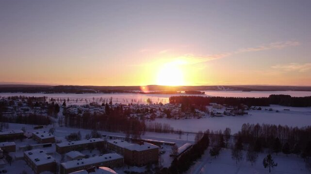 Winter sunset aerial over snow-covered suburb and a frozen lake in the north of Sweden