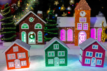 Close-up of three Christmas houses against the backdrop of fir trees, large Christmas houses and a Christmas wreath