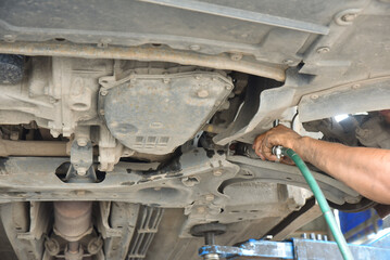 Male car mechanic with oil-stained hands fixing a car's undercarriage.