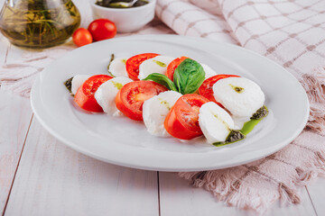 Caprese salad with tomatoes, mozzarella cheese, pesto and basil on white plate