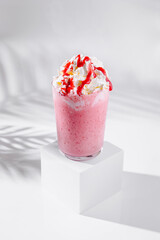 Strawberry milkshake with whipped cream and syrup standing on white cube