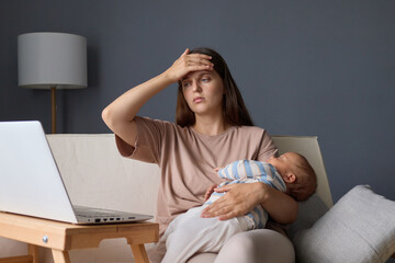 Tired exhausted woman sitting at home with her baby working on her laptop and browsing the internet while her infant sleeping feeling unwell touching her painful forehead suffering headache