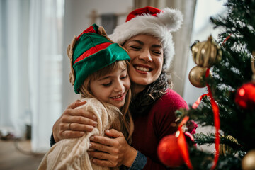 Happy mother embracing her cute daughter on the sofa in in the living room at Christmas