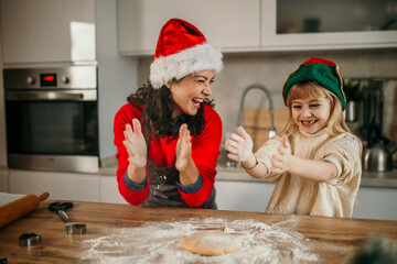 Happy mother and daughter clapping with hands and playing with flour at home while cooking for a Christmas