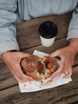 Hands holding pecan cinnamon roll on a wooden picnic table outdoors