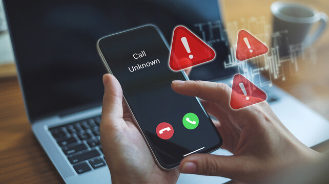 Person holding a smartphone displaying an unknown incoming call with warning signs, indicating potential scam or spam calls.