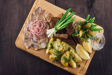 Sliced herring with potatoes and onions on wooden board