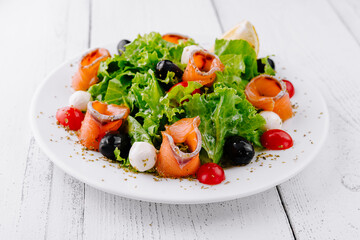 Delicious salad with smoked salmon, mozzarella and cherry tomatoes on white table