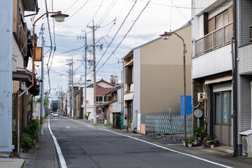 A narrow and quiet Japanese residential street, lined with two-story old and weathered houses....