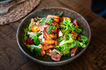 Gebratener Lachs auf Salat angerichtet im Teller auf Holztisch im Restaurant Hotel