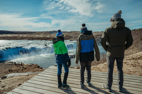Family in winter gear viewing Faxafoss waterfall, Iceland, blue sky