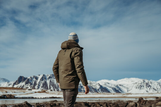 Man in winter clothing overlooking snow-capped mountains at Ytri Tunga
