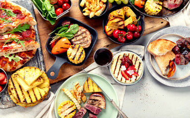 Table with grilled food. Pizza, corn, tomatoes, peppers, cooked meat. BBQ time