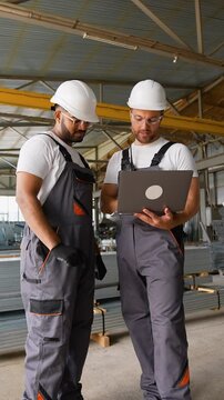 Caucasian foreman and Indian worker with laptop in warehouse metal profile