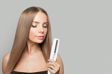 Woman brunette lady with straight hair holding straightening iron on white background. Female...