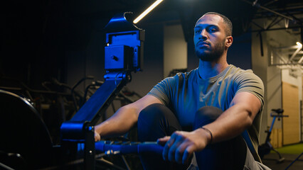 Sport determination hard exercise with equipment in sportive club muscles workout African American strong man sporty male guy athlete sportsman bodybuilder in gym pulling rope rowing machine sitting