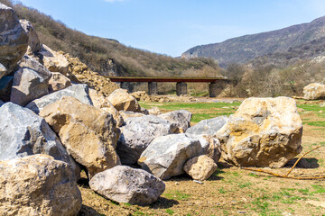 Huge stones in the meadow. Iron bridge over the river in the gorge. Mountains in the background