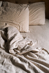 Empty bed covered wrinkled bedding and pillows in cozy bedroom at nighttime.