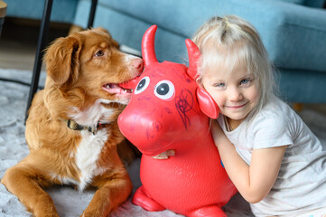 Young girl having fun with her toy and nova scotia toller dog friend