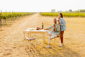 Romantic picnic in a sunlit vineyard featuring a couple enjoying wine and a gourmet platter among the vines during golden hour