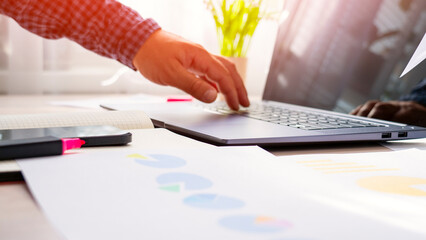 A man is typing on a laptop with a green plant in the background. The laptop is open to a document with graphs and charts. Concept of productivity and focus as the man works on his project